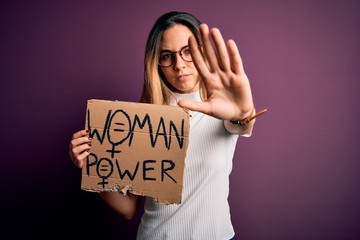 Young beautiful blonde woman with blue eyes asking for women rights holding banner with open hand...