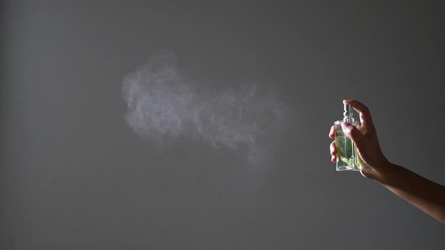 Slow motion, spraying fragrance with scent particles. Perfume bottle in hand