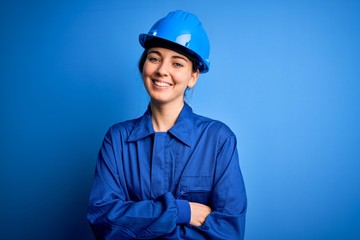 Young beautiful worker woman with blue eyes wearing security helmet and uniform happy face smiling...