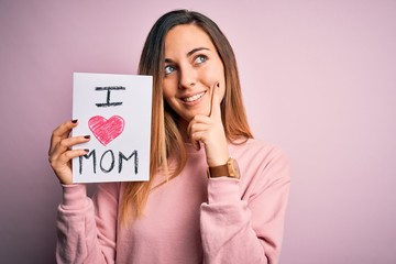 Young beautiful woman holding paper with love mom message celebrating mothers day serious face...