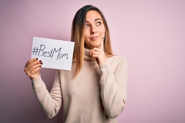 Young beautiful woman holding paper with best mom message celebrating mothers day serious face...