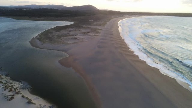 Aerial view of Beautiful beach with crushing waves on shoreline. Sandy beach at sunset from above. Valdovinos, Galicia Spain. Drone footage track out