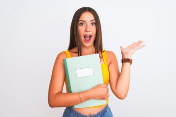 Young beautiful student girl holding notebook standing over isolated white background very happy and excited, winner expression celebrating victory screaming with big smile and raised hands