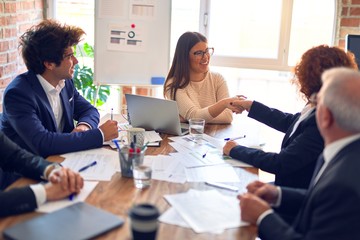 Group of business workers smiling happy and confident in a meeting. Speaking with smile on face working together shaking hands for agreement at the office.