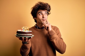 Young handsome man holding birthday cake standing over isolated yellow background serious face...