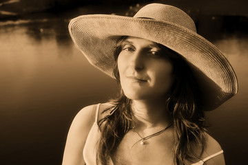 A young woman in a straw hat on the background of water in the rays of the setting sun, sepia