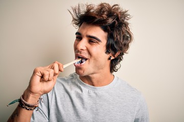 Young handsome man smiling happy. Standing with smile on face whasing tooth using toothbrush over isolated white background