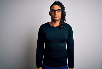 Young handsome african american man with dreadlocks wearing casual t-shirt and glasses with serious expression on face. Simple and natural looking at the camera.
