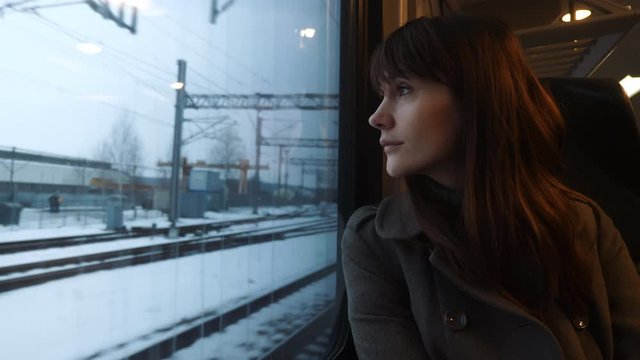 Portrait of young calm thoughtful beautiful Caucasian woman looking out of train window passenger seat slow motion.
