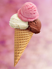 Chocolate, strawberry and vanilla ice cream scoops on cone with pink background