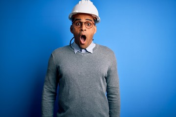 Young handsome african american engineer man with dreadlocks wearing safety helmet afraid and shocked with surprise expression, fear and excited face.
