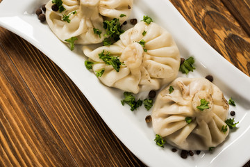 close up view of delicious Khinkali with cilantro on plate on brown wooden table
