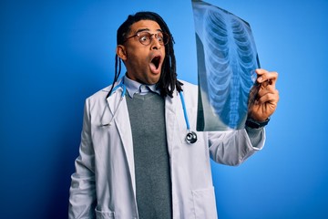 Young african american afro doctor man with dreadlocks holding chest lung xray scared in shock with a surprise face, afraid and excited with fear expression
