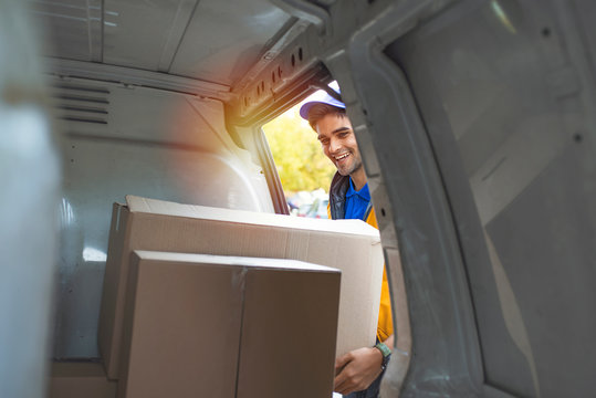 Man Loading Moving Boxes In To His Car. View From The Car Trunk. Close-up Of  Delivery Man Carrying Cardboard Box. Getting His Deliveries Out. Shot Of A Courier Checking His Deliveries In His Van