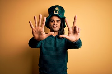 Young african american man wearing green hat with clover celebrating saint patricks day showing and pointing up with fingers number eight while smiling confident and happy.