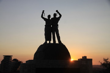 pomnik afrykańskich niewolników z zerwanymi kajdanami na rękach na tle zachodzącego słońca w afryce - obrazy, fototapety, plakaty