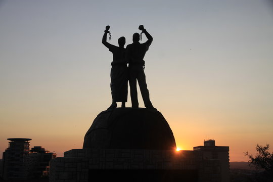 pomnik afrykańskich niewolników z zerwanymi kajdanami na rękach na tle zachodzącego słońca w afryce