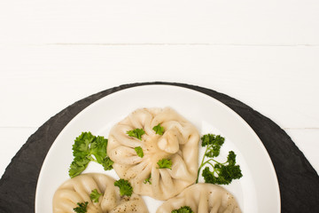 top view of delicious Khinkali with cilantro on plate on white wooden table