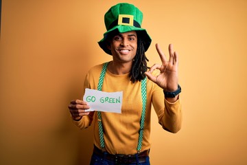 Young african american man wearing green hat holding banner celebrating saint patricks day doing ok sign with fingers, excellent symbol
