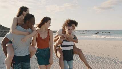 Two happy young men giving their girlfriends piggyback rides at the beach. Group of friends enjoying beach holidays.