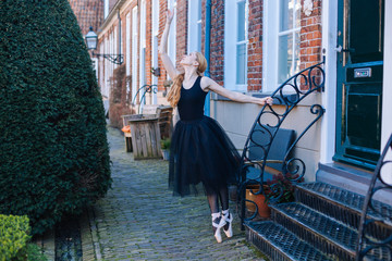 Young ballerina woman with red hair in ballet costume and pointe shoes is in beautiful pose dancing on street. Ballerina is posing in the streets. Girl dancing outdoors. Street ballet and performance