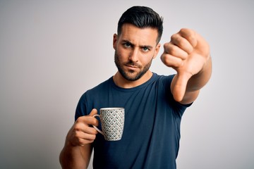 Young handsome man drinking a cup of hot coffee over white isolated background with angry face,...
