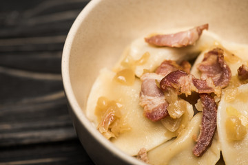 close up view of delicious varenyky with cracklings in bowl on black wooden table