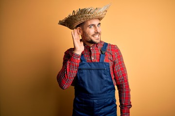 Young rural farmer man wearing bib overall and countryside hat over yellow background smiling with...