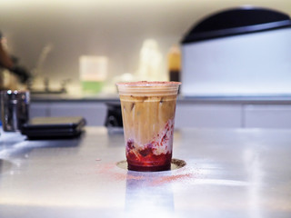 Hand holds a plastic glass of iced coffee latte with layer of jam strawberry. selective focus.
