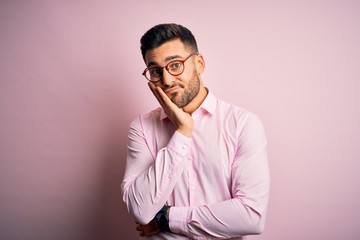 Young handsome man wearing elegant shirt and glasses standing over pink background thinking looking tired and bored with depression problems with crossed arms.