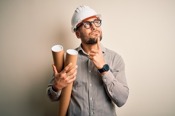 Young architect man wearing contractor helmet holding project paper plan over isolated background...