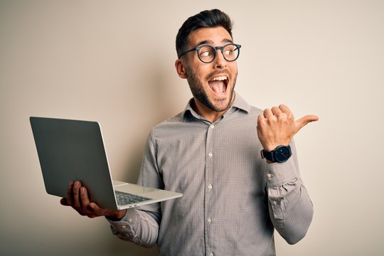Young business man wearing glasses working using computer laptop pointing and showing with thumb up to the side with happy face smiling