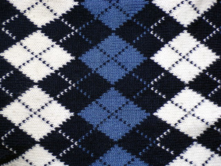 The texture of the sweater with diamonds and borders. Warm winter sweater as a textile abstract background with space copying. Knitwear. Handmade sweater. Cardigan.