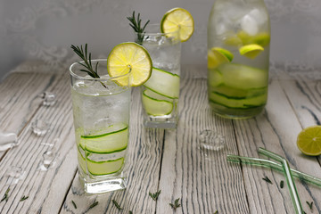 Refreshing detox water with ice cubes, lime, cucumber and rosemary on light wooden rustic background