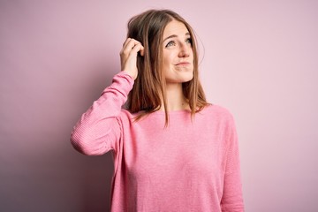 Young beautiful redhead woman wearing casual sweater over isolated pink background confuse and wondering about question. Uncertain with doubt, thinking with hand on head. Pensive concept.