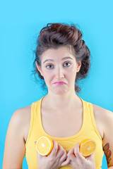 Beautiful brunette in yellow top holds lemons like tits over blue background, beauty concept