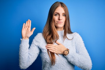 Young beautiful redhead woman wearing casual sweater over isolated blue background Swearing with...