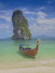 Fototapeta na wymiar view seaside of a long-tail boat floating in blue-green sea with cliff mountain and cloudy sky background, Ko Poda island, Krabi, southern of Thailand.