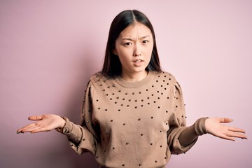 Young beautiful asian woman wearing fashion and elegant sweater over pink solated background...