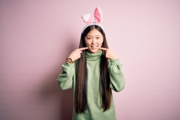 Young asian woman wearing cute easter bunny ears over pink background smiling cheerful showing and pointing with fingers teeth and mouth. Dental health concept.