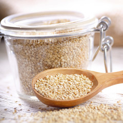 Raw organic superfood gluten free quinoa seeds in wooden spoon and glass airtight jar on kitchen table closeup