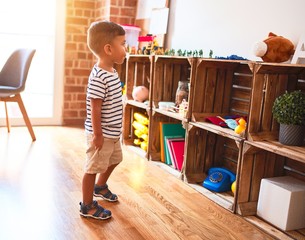Beautiful toddler boy standing at kindergarten with lots of toys