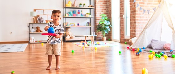 Beautiful toddler boy playing tennis with red racket and ball at kindergarten