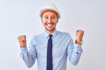 Young business man wearing contractor safety helmet over isolated background celebrating surprised and amazed for success with arms raised and open eyes. Winner concept.