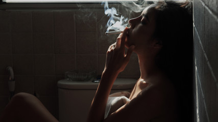 Asian woman inhaling and cigarette vaping. Female secretly smoking in bathroom at home. Concept of quit smoking and anti cigarette.