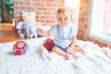 Beautiful toddler sitting on the blanket with colorful balls at kindergarten