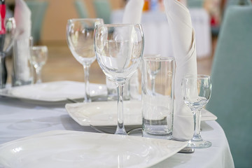 The table in the restaurant is served for dinner. On a table with a white tablecloth, empty wine glasses, a plates, napkins. Selective focus
