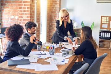 Group of business workers smiling happy and confident. Working together with smile on face. Middle age beautiful woman standing explaining documents at the office
