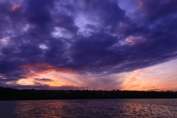 Obraz premium Dramatic stormy sky with cumulonimbus at sunset. Colorful clouds over a valley to the water's edge. Peaceful landscape in the countryside.