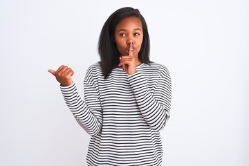 Beautiful young african american woman wearing winter sweater over isolated background asking to be quiet with finger on lips pointing with hand to the side. Silence and secret concept.